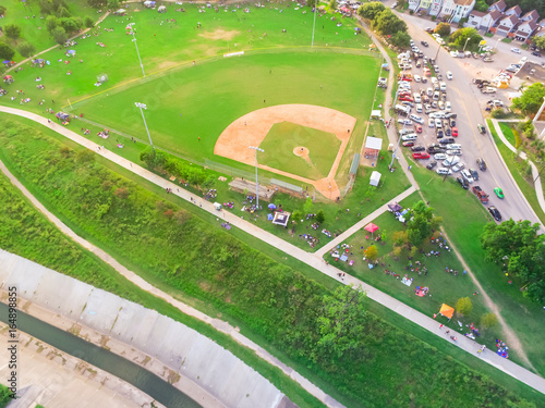 Aerial view a baseball stadium in residential neighborhood near downtown Houston, Bayou river. Full cars at outdoor parking lots and crowd of people/audience sitting on grass, folding chairs and tents