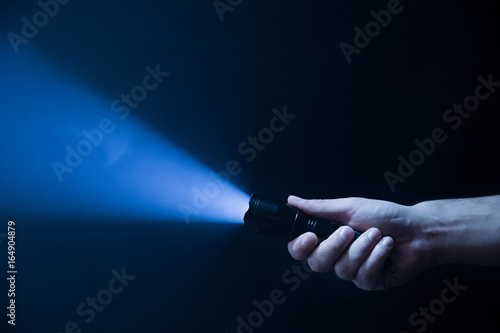 The flashlight in the man's hand from the right side of the frame in black and blue color isolated on black background