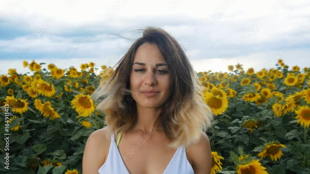 Portrait of a young woman in a field of sunflowers. The wind blows her hair. Thunderclouds on the background. Portrait of a young woman in a field of sunflowers. The wind blows her hair. Thunderclouds on the background.