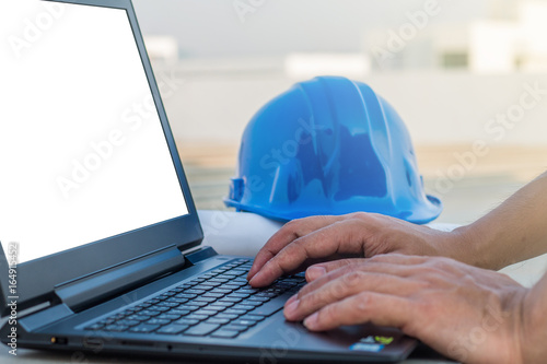 The human hands typing a keyboard on laptop with white screen isolated at construction site