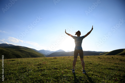 cheering woman open arms to sunset at mountain top