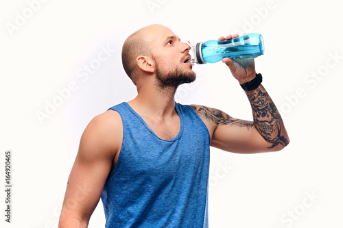 Shaved head sporty male drinks water.