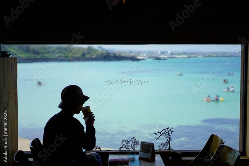 Woman who is drinking coffee from the window where the blue sea is visible.