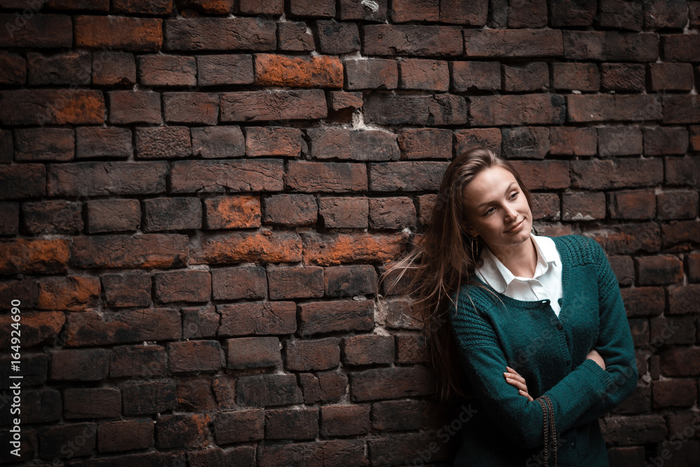 Young stylish casual woman standing near brick dark wall, ancient, looking away, copy space,outdoor