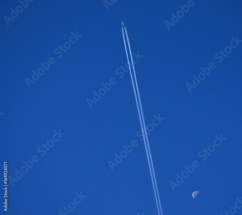 Airplane crossing the blue sky at high altitude and the waning moon