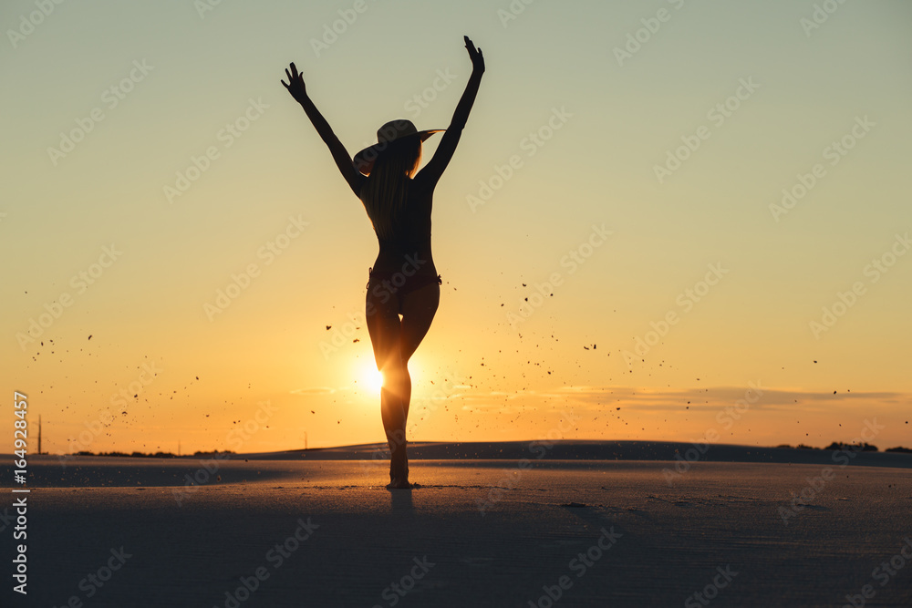 Silhouette of woman throws sand in gold desert at sunset