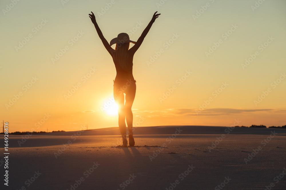 Silhouette of freedom woman with raised hands in gold desert at sunset