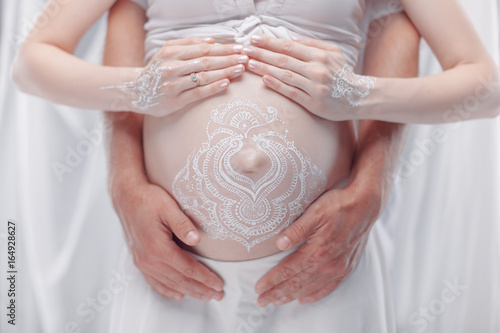 Pregnant belly closeup with white henna painting in boho style.
