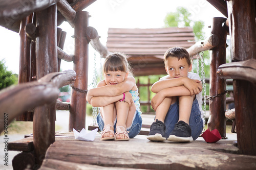 Two small kids sitting in a wooden house outdoors on sunny summer day photo