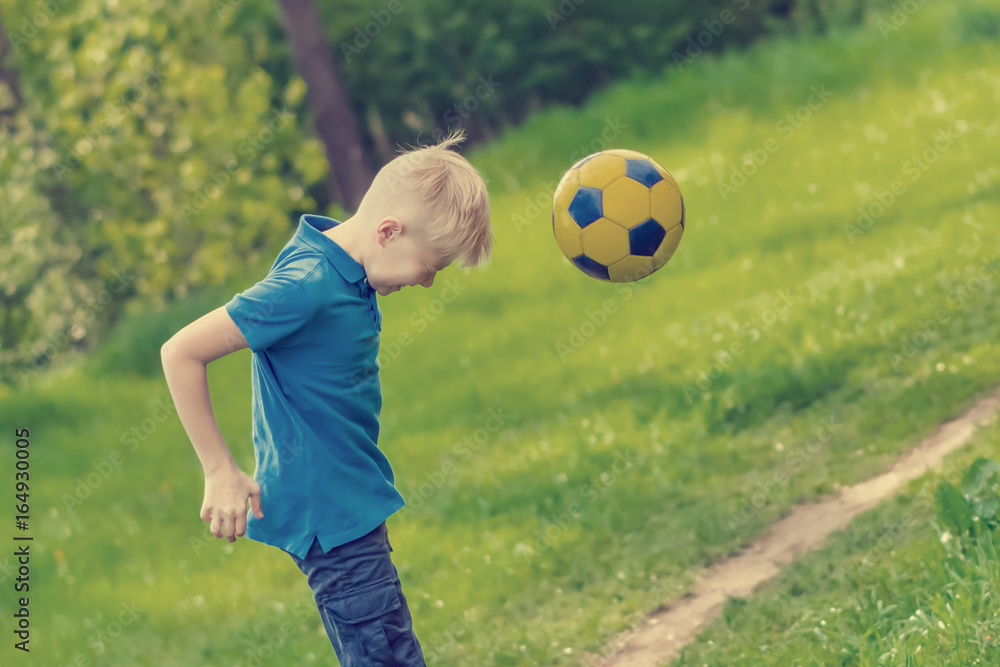 Blond boy blows his head off a soccer ball in the park