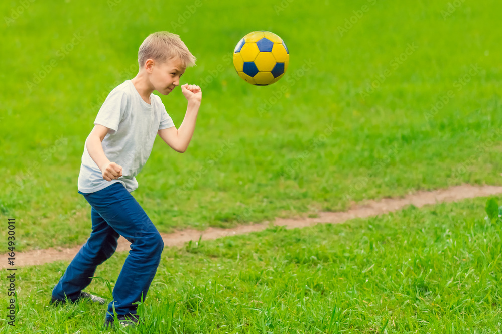 Blond boy in a white T-shirt playing with a soccer ball in the park. Toned Blond boy in a white T-shirt playing with a soccer ball in the park. Toned