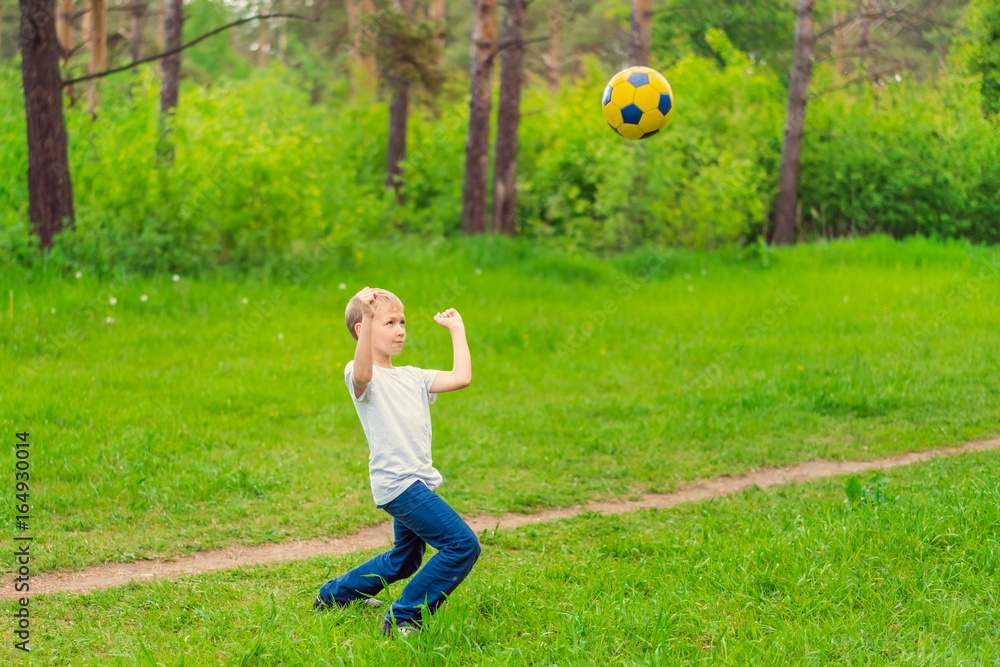 Obraz premium Blond boy in a white T-shirt playing with a soccer ball in the park