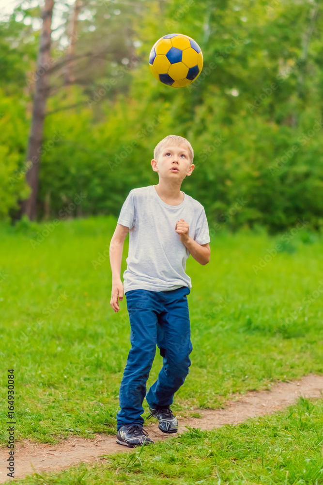 Obraz premium Blond boy in a white T-shirt tossed a soccer ball in the park