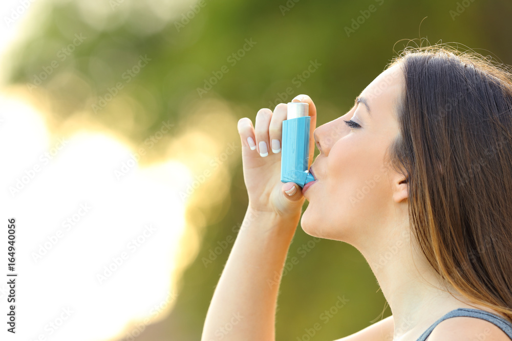 Woman using an asthma inhaler outdoors Woman using an asthma inhaler outdoors