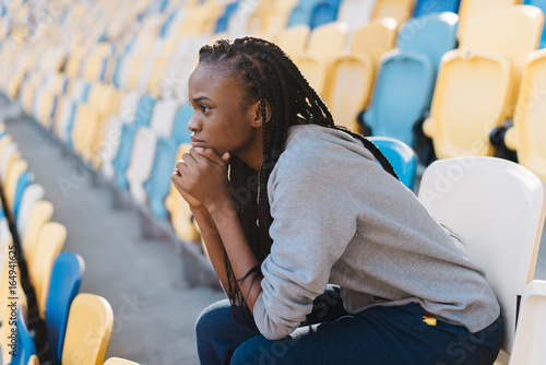 Emotiontal portrait of the afro-american girl worrying about the match on the stadium.