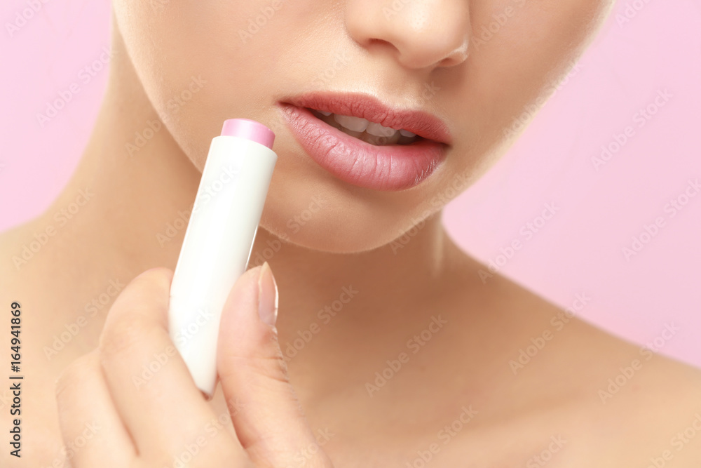 Closeup view of beautiful young woman applying lipstick, color background