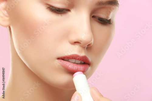 Closeup view of beautiful young woman applying lipstick  color background