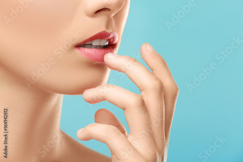 Closeup view of beautiful young woman with natural makeup touching lips on color background