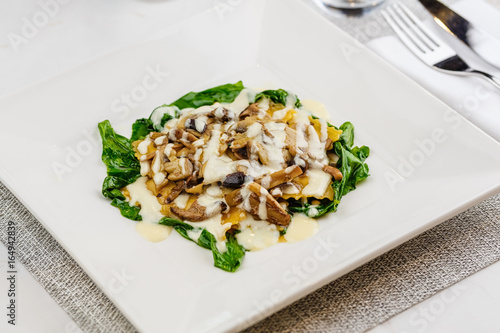 Italian ravioli with fresh roasted mushrooms and creamy parmesan cheese sauce decorated with spinach on white plate. photo