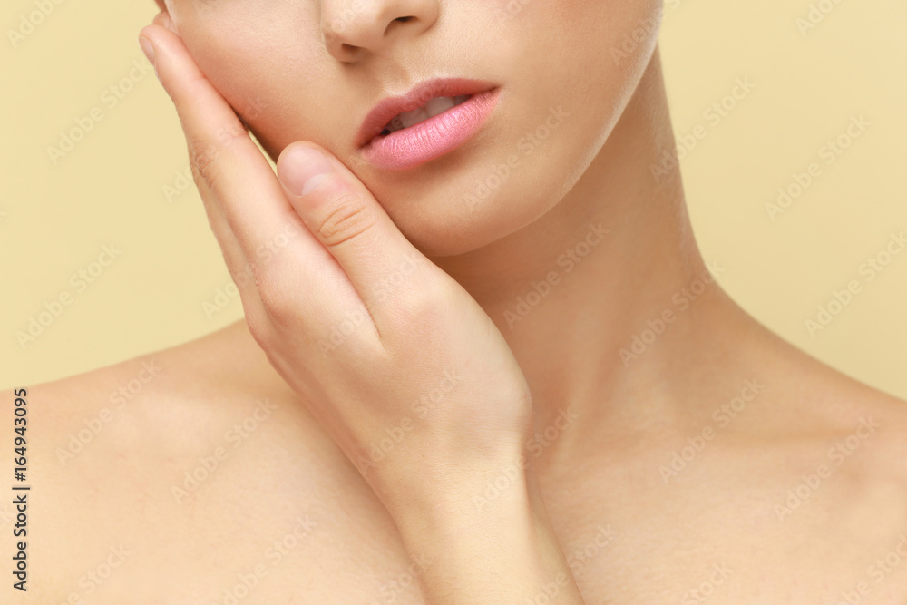 Closeup view of beautiful young woman with natural lips makeup touching face on color background Closeup view of beautiful young woman with natural lips makeup touching face on color background