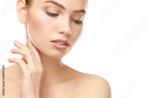 Beautiful young woman with natural lips makeup touching neck on white background