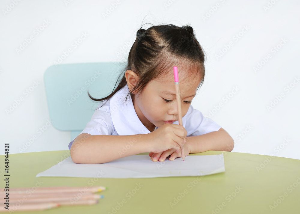 Asian child in school uniform with pencil writing on table isolated on white background. Asian child in school uniform with pencil writing on table isolated on white background.