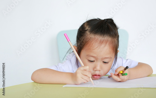 Asian child in school uniform with pencil writing on table isolated on white background. photo