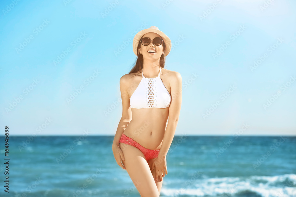 Beautiful young woman in bikini near sea on sunny day