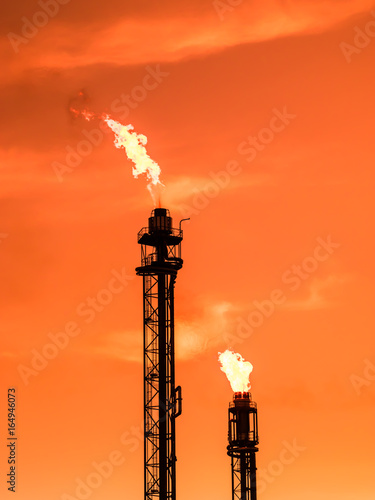 Refinery chimney with fire at orange sunset