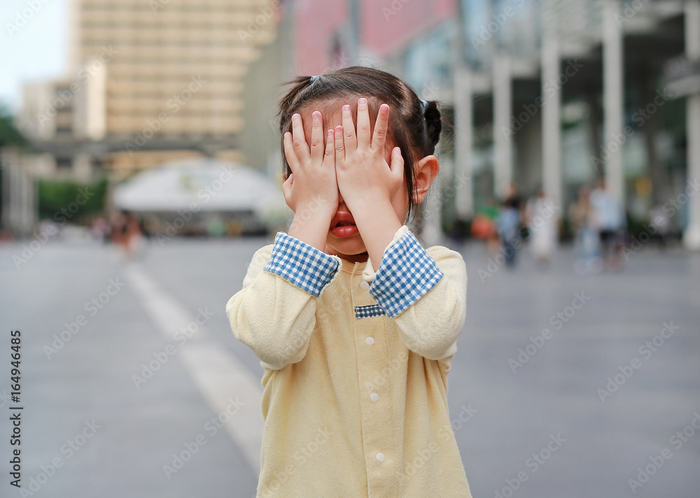 Asian little girl cover her face with her hands.
