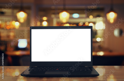 open laptop with white screen on wooden table in front of abstract blurred restaurant lights background. © tomertu
