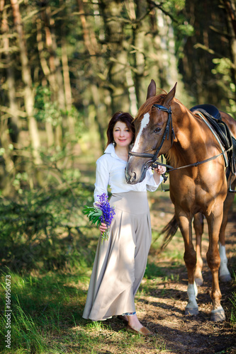 woman with a bouquet of flowers walks with the favourite horse in the wood