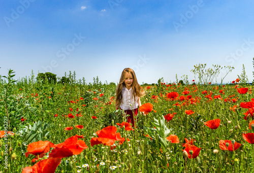 Cute little girl playing in red poppies field summer day, beauty and happiness