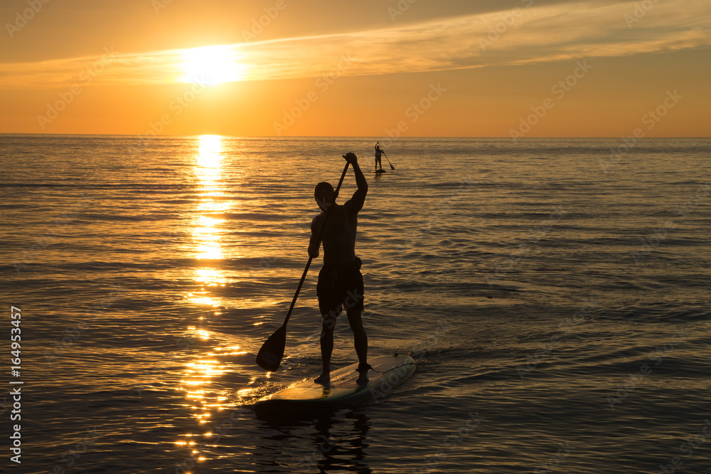 Golden setting sun with young man paddling in foreground.