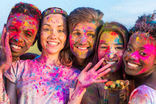happy young multiethnic friends having fun with colorful powder at holi festival of colors