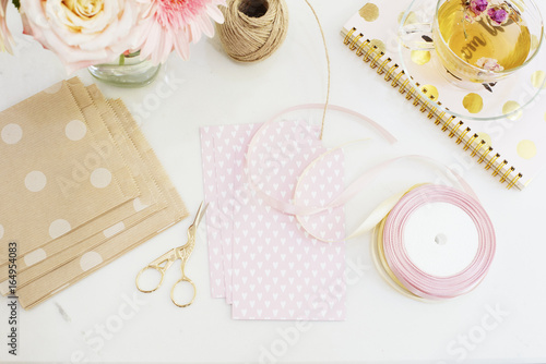 Handmade, craft concept. Materials for making string bracelets and handmade goods packaging - twine, ribbons. Freelance workspace in flat lay style with flowers, rose tea, notebooks  photo