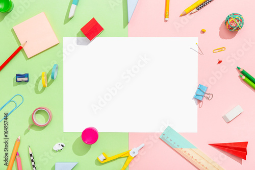 Blank sheet of paper on a colorful workspace with school supplies. Flat lay.