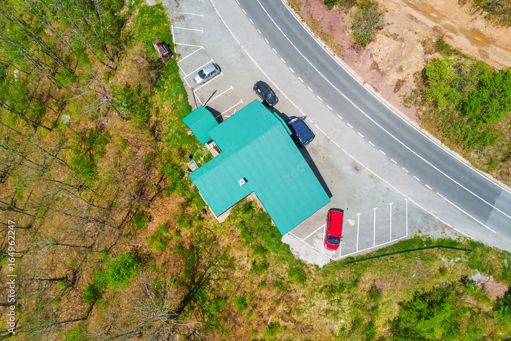 Fototapeta premium Building with a green roof and parked cars on the edge of the road in the forest, top view