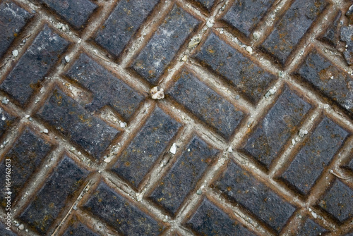 Closeup / textures of an old rusty iron manhole, consisting of small parallel rectangles as in a chessboard, near a Swiss mountain dam, ruined by the weather of the seasons, Alps, Switzerland