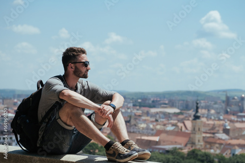 Man traveler with backpack explores the city looking at the panoramic view of the city and the coast. The concept of travel is discovering new places photo