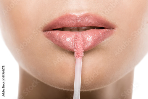 close up view of beautiful woman applying pink lipgloss on lips, isolated on white photo
