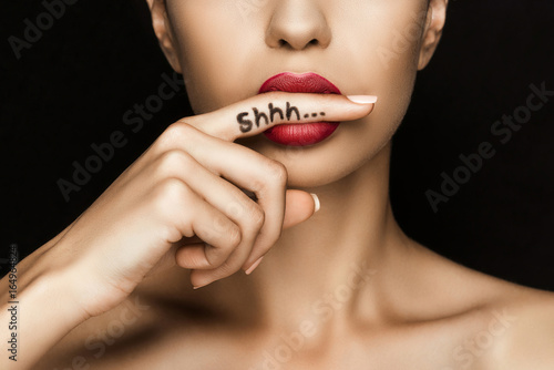 cropped view of seductive woman with red lips showing shh symbol, isolated on black photo