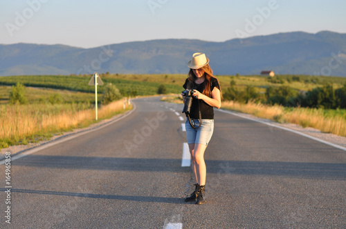 Woman with a camera on the middle of the road in mountains. Forty Years old woman on the road