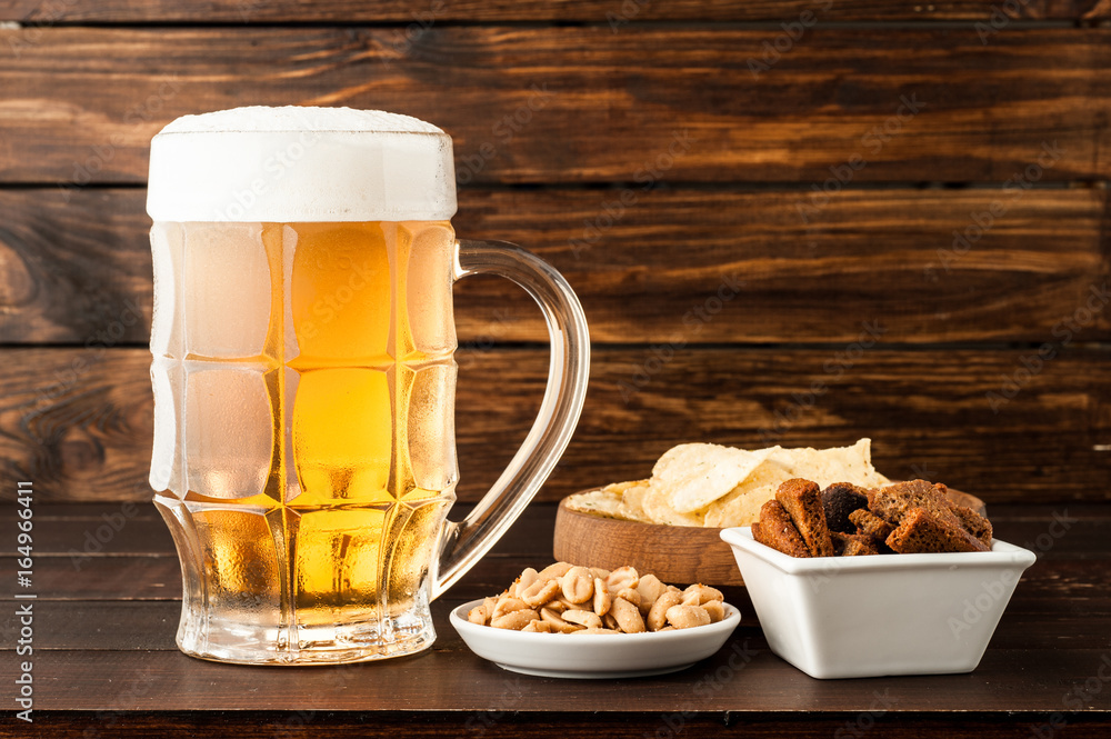 glass of cold frothy lager beer and snacks on wooden table glass of cold frothy lager beer and snacks on wooden table