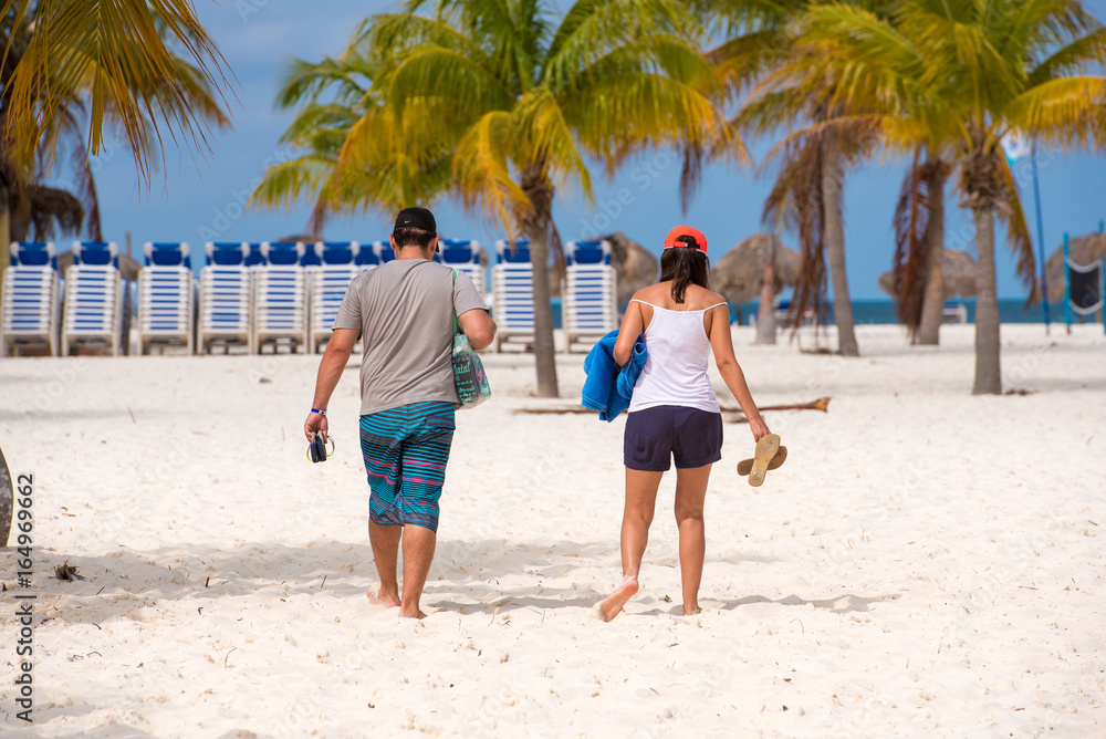 A man and a woman go to Playa Sirena beach, Cayo Largo, Cuba. Back view.