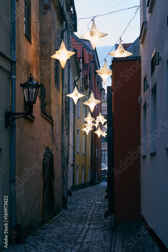 Narrow street lit by streetlights in the form of stars in the old town in Riga