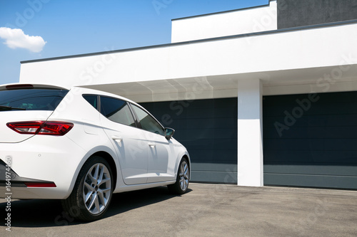 White car in front of modern house waiting to enter in the garage with large garage door