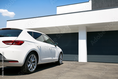 White car in front of modern house waiting to enter in the garage with large garage door © concept w