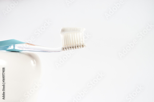 Close-up of a toothbrush with toothpaste on white healthy ceramic tooth model isolated on white. Dental hygiene and care