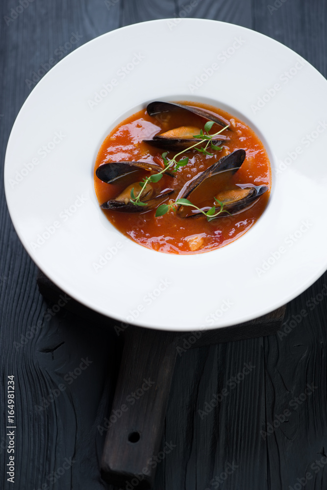 Tomato soup with mussels served in a white plate over black wooden background, studio shot